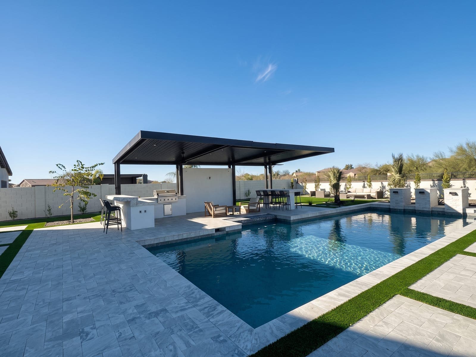 Black cantilever with VEER-Batten roof panels over an outdoor kitchen beside a pool