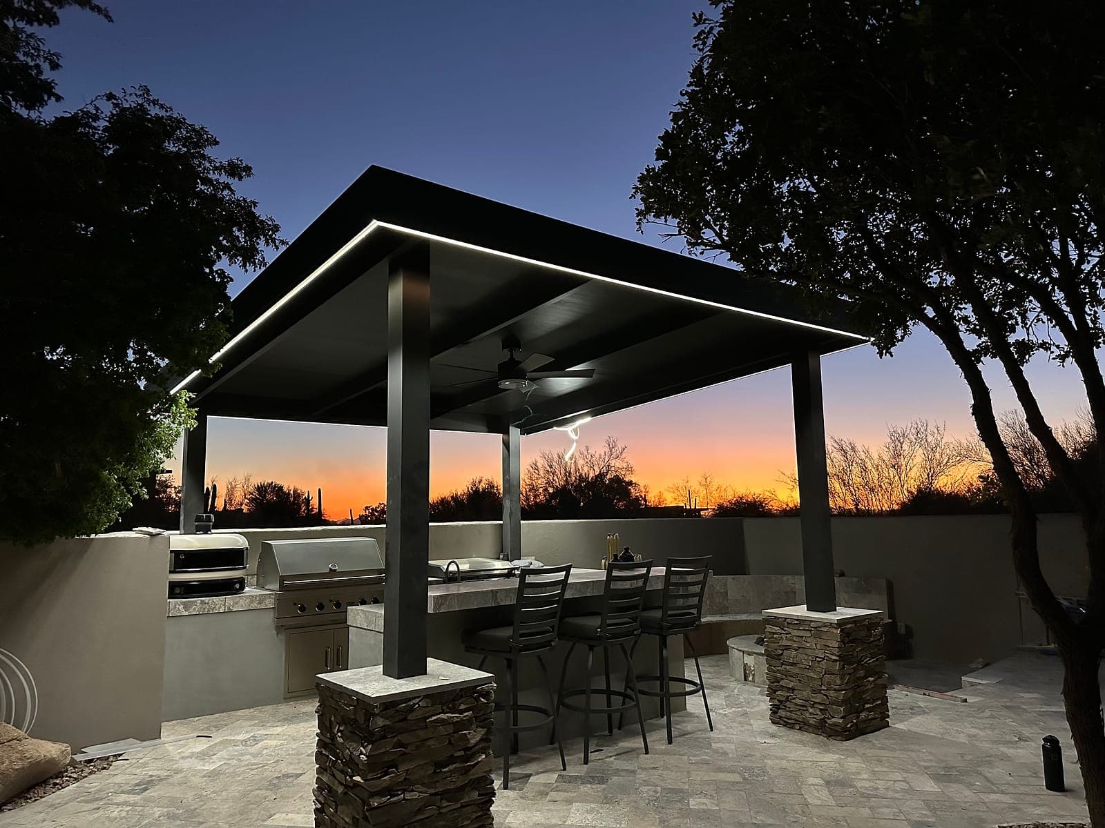 Freestanding cover with black VEER-Smooth panels over an outdoor kitchen at sunset