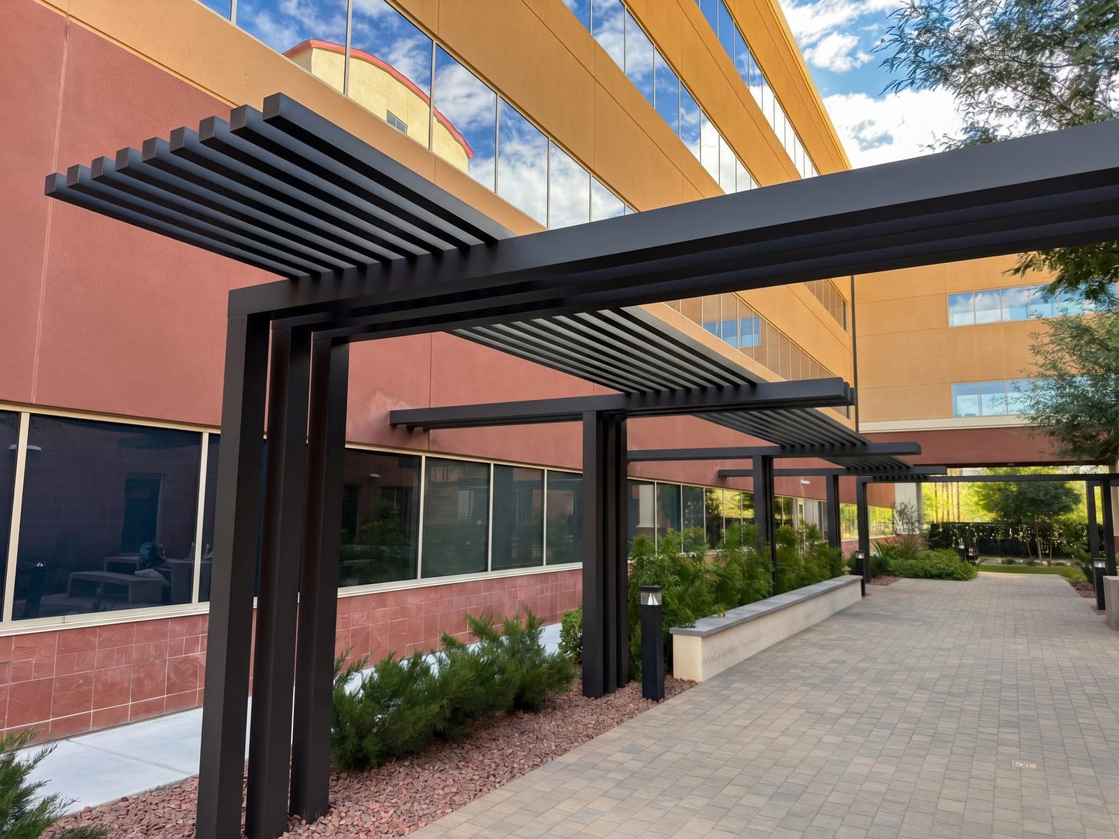 Espresso aluminum architectural feature with grouped posts and long beams topped with 2-inch lattices, along a courtyard at Southern Hills Hospital