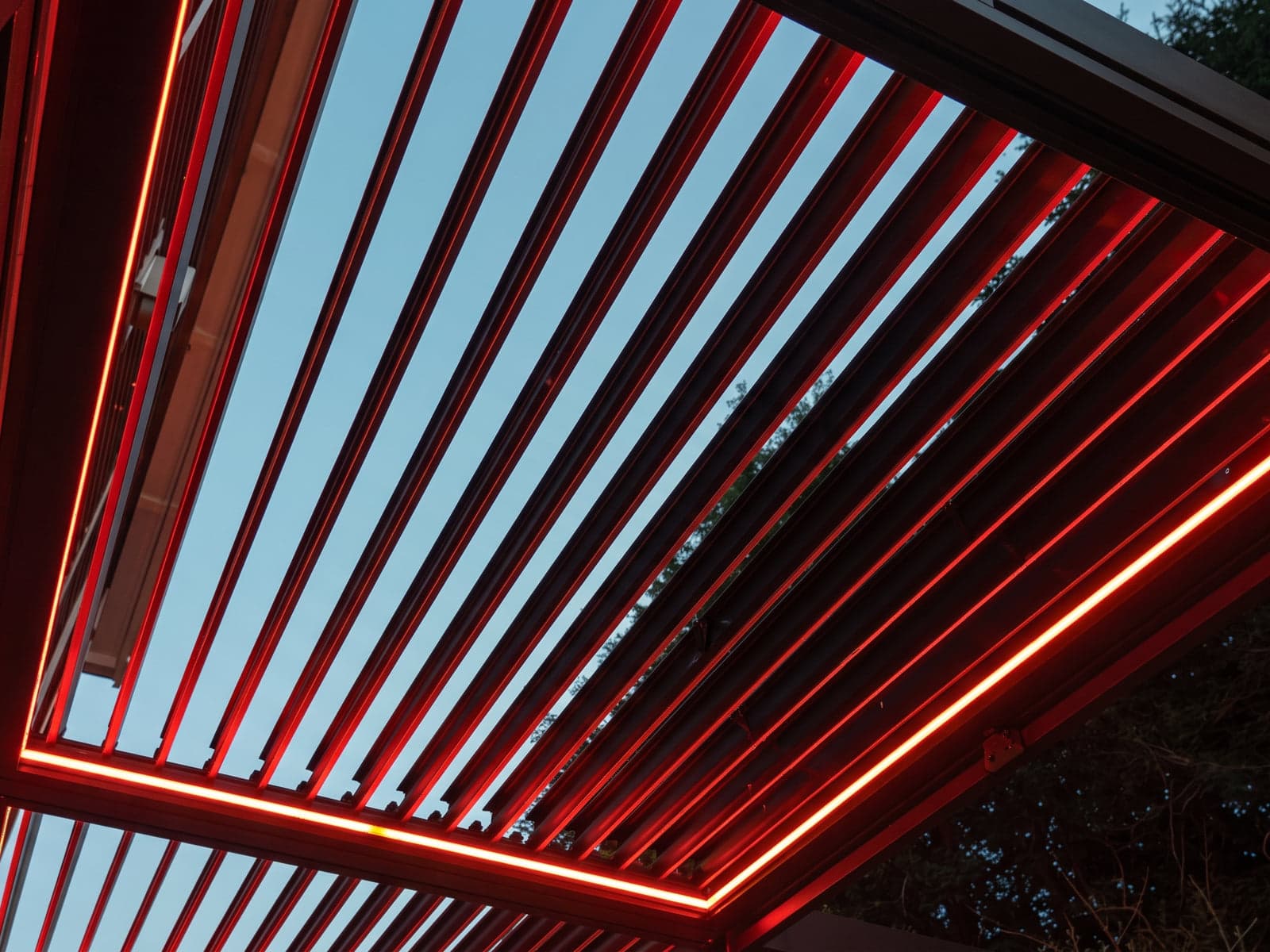 View from below of a louvered roof outlined with red LED strip lights against the evening sky.