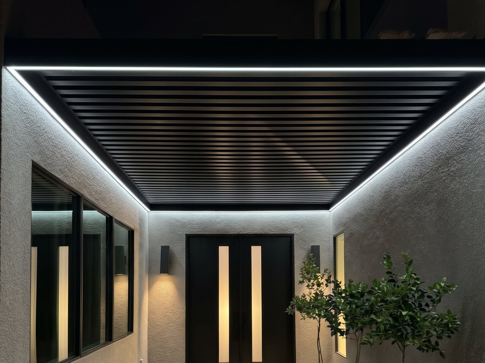 Slatted roof over an entry walkway at night, outlined with white LED strip lights.