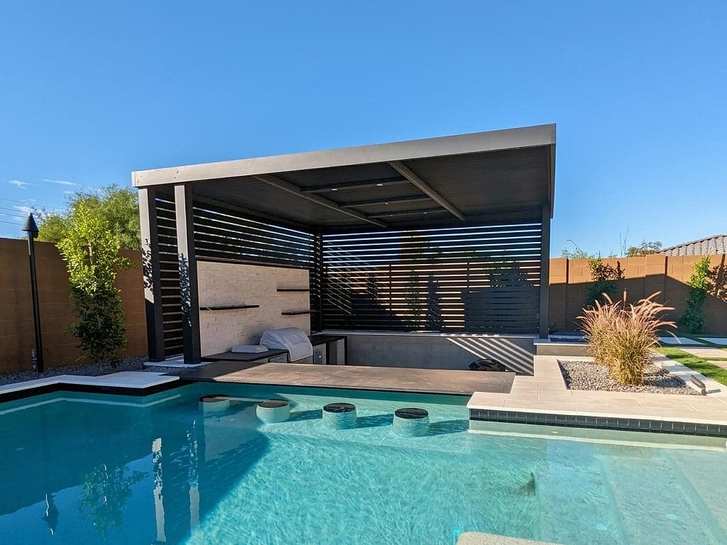 Pergola with posts on three corners, a black VEER roof and lattice privacy walls over a sunken kitchen by a pool